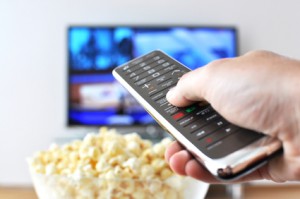 Remote control in the hand against pop-corn and TV-set